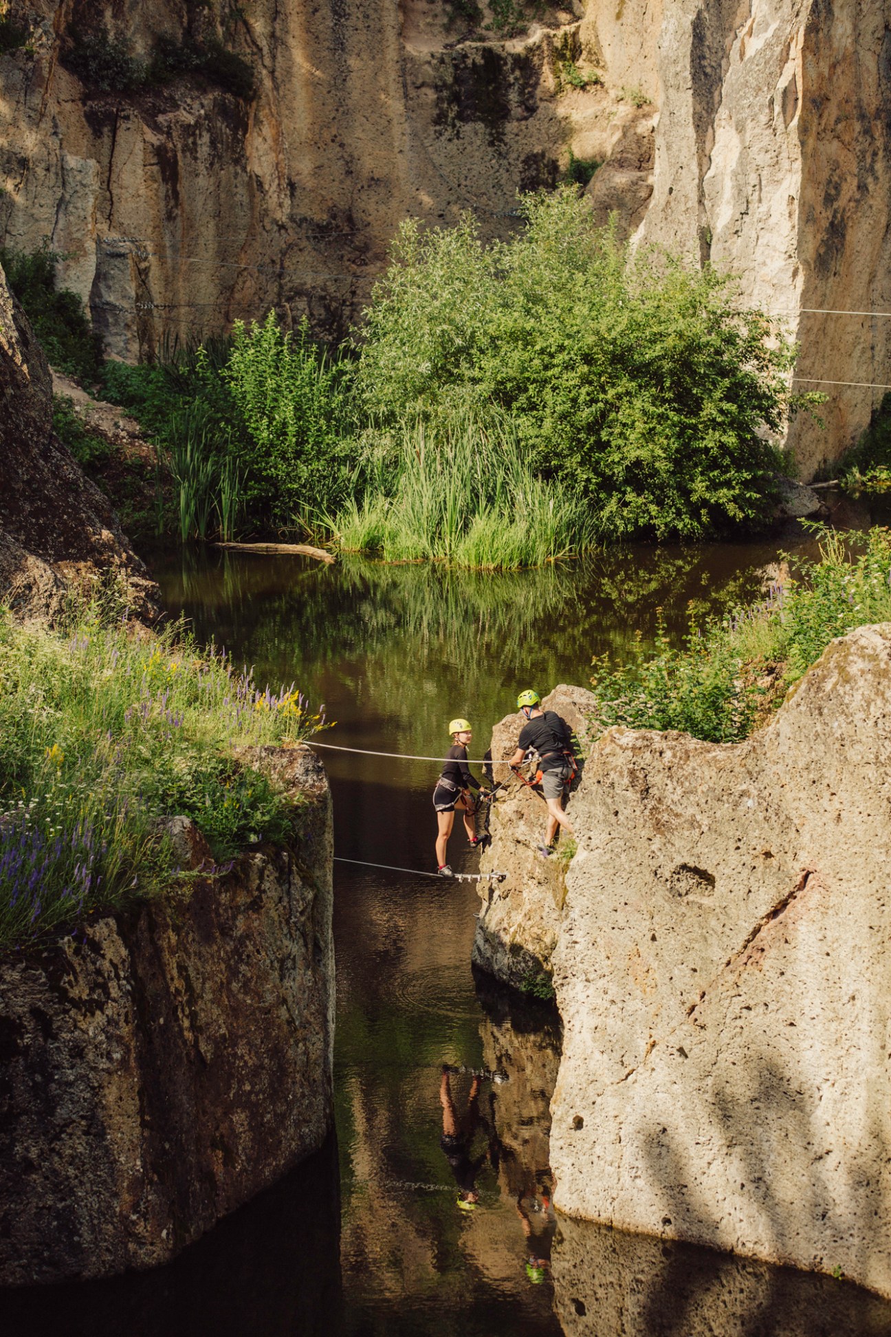 Two people canyoning through a narrow rocky gorge with water and safety ropes in the Zemplen Mountains