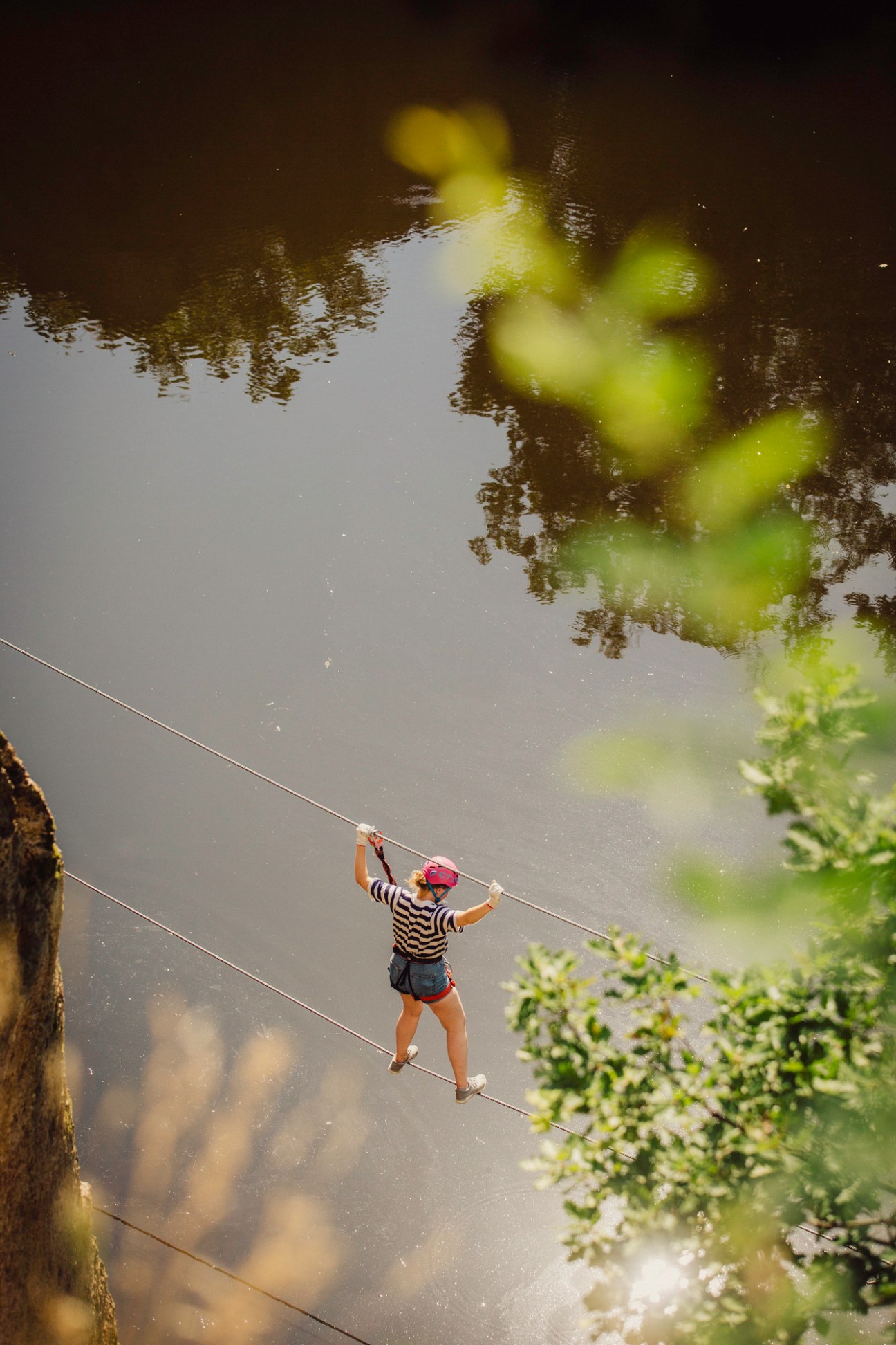 Person crossing rope bridge high above water in adventure park setting