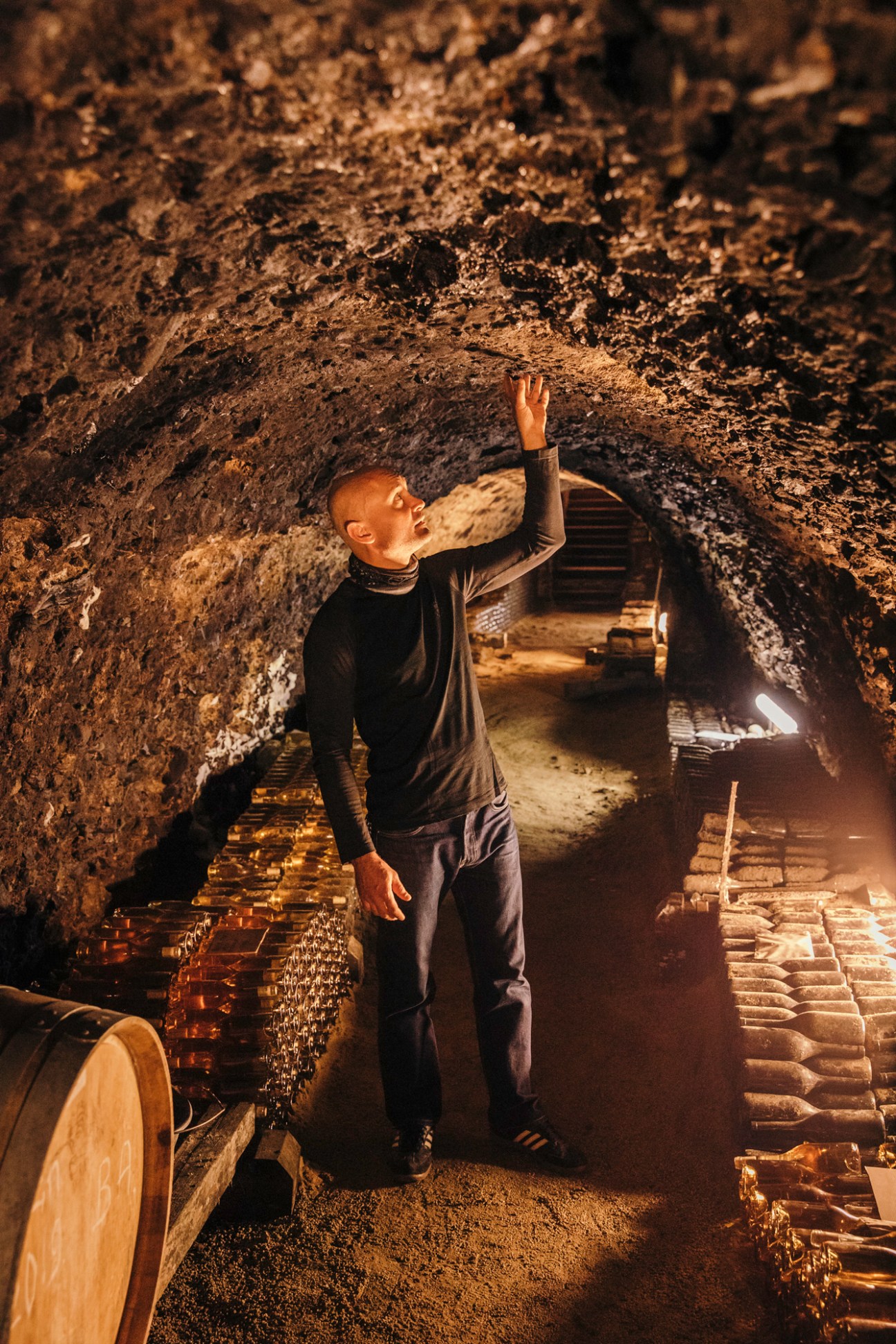 Winemaker Endre Demeter examining wine cellar ceiling in underground cave with stone walls and wooden barrels