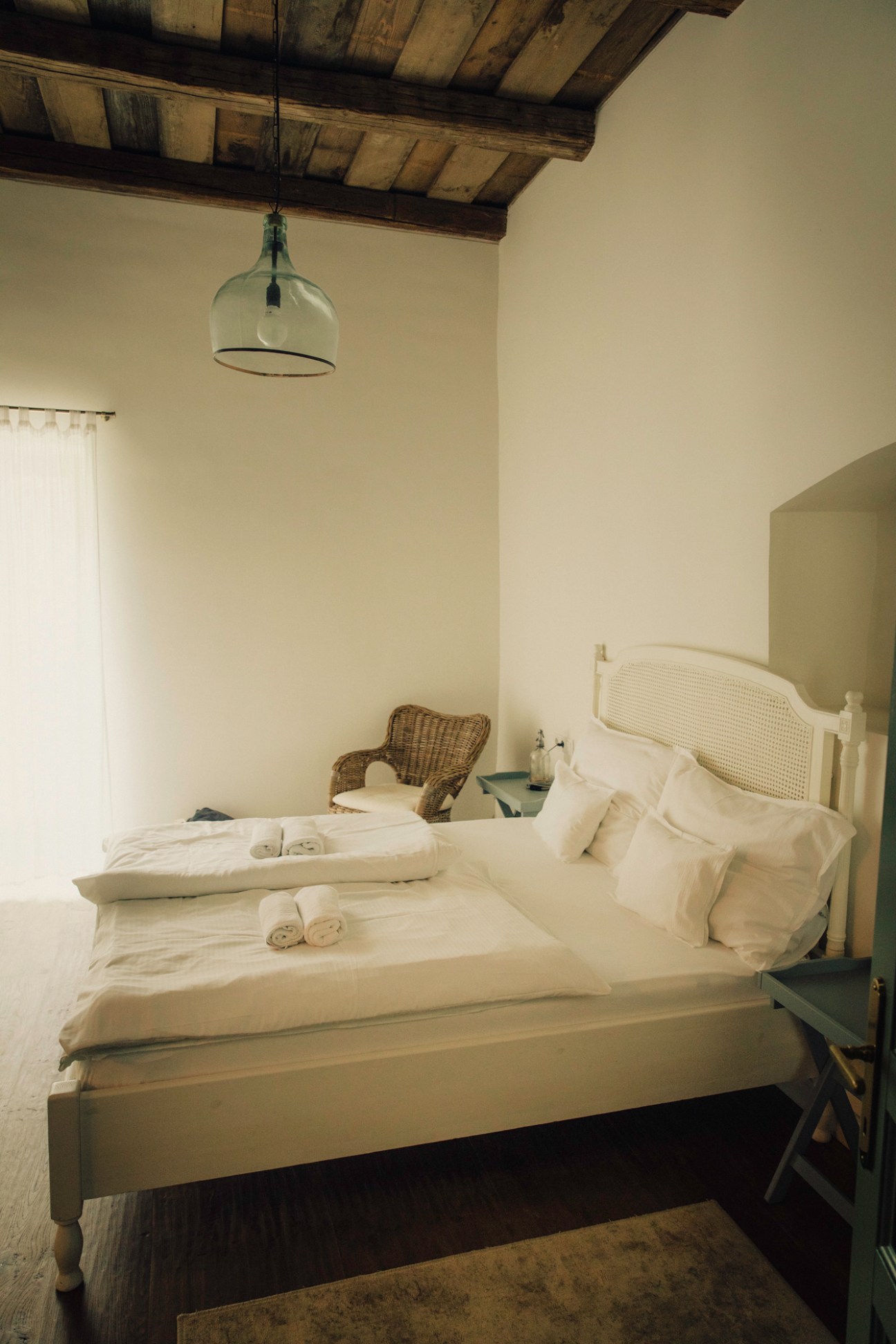 Guest room at Hotel R40 with white bed, wicker chair, exposed wooden ceiling beams and glass pendant light