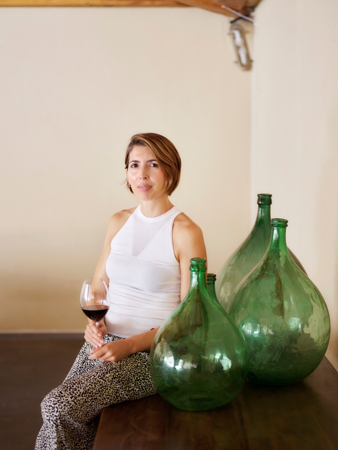 Valentina Argiolas at her family's winery holding a wine glass next to large green glass demijohns