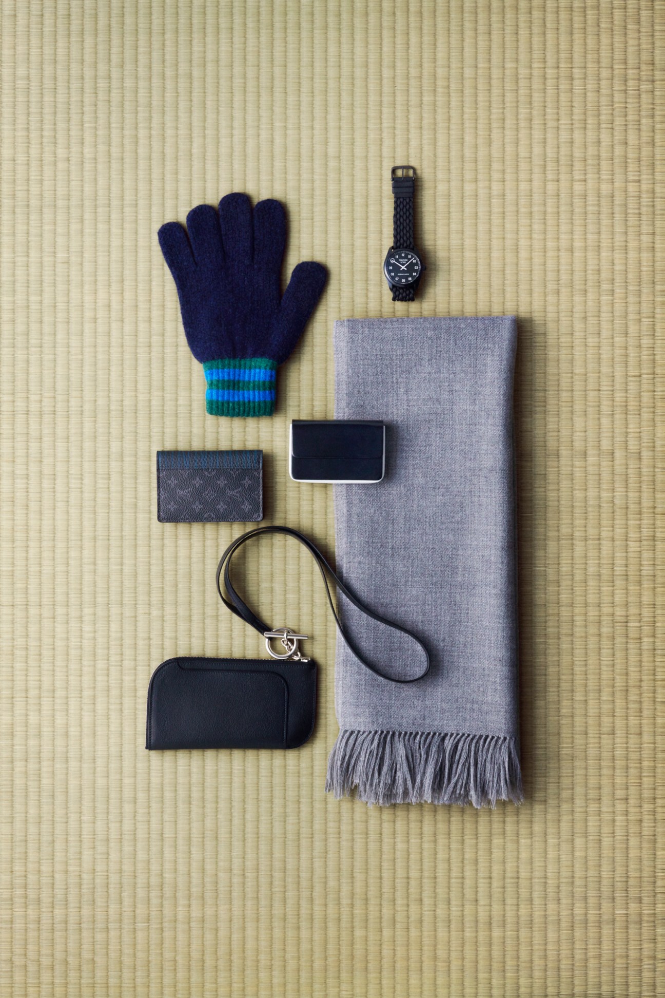 Navy gloves, watch, gray scarf, phone, and black accessories arranged on woven mat surface