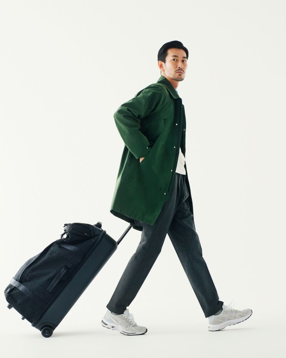 Man in green Goldwin coat and dark trousers pulling a black Porter suitcase.