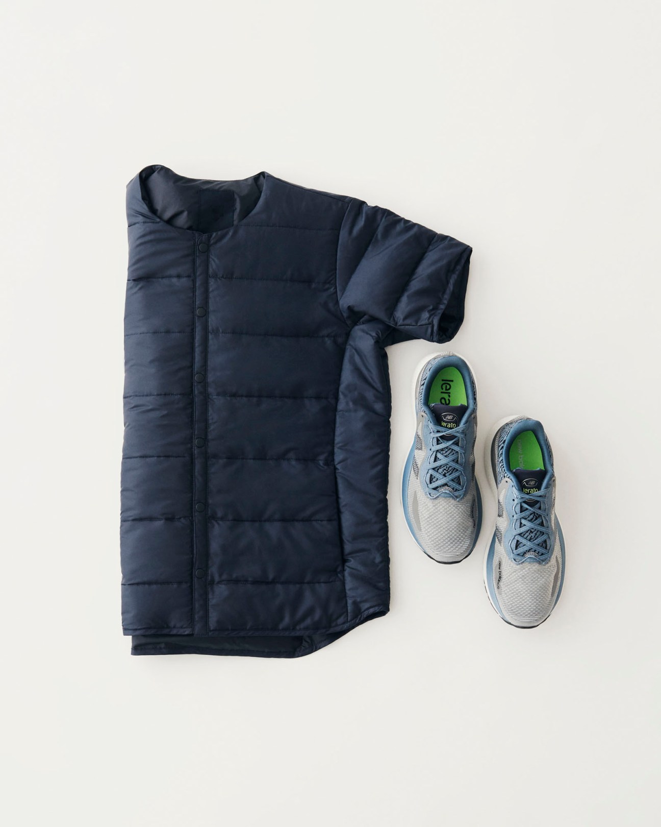 Navy down jacket and grey New Balance trainers with green insoles arranged on white background