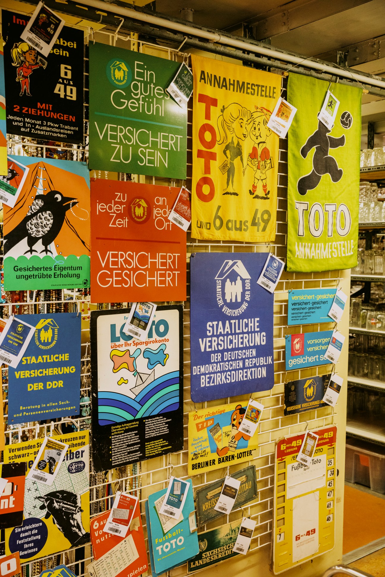 Display of colorful vintage East German promotional posters and lottery advertisements hanging on wire grid