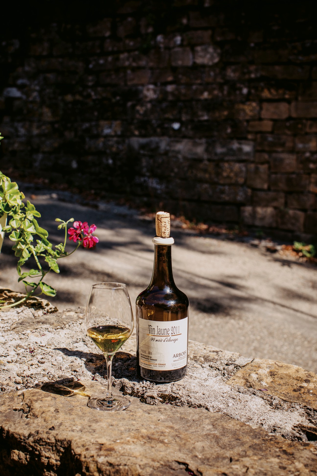 Bottle of vin jaune yellow wine from Bénédicte and Stéphane Tissot winery with glass on stone surface