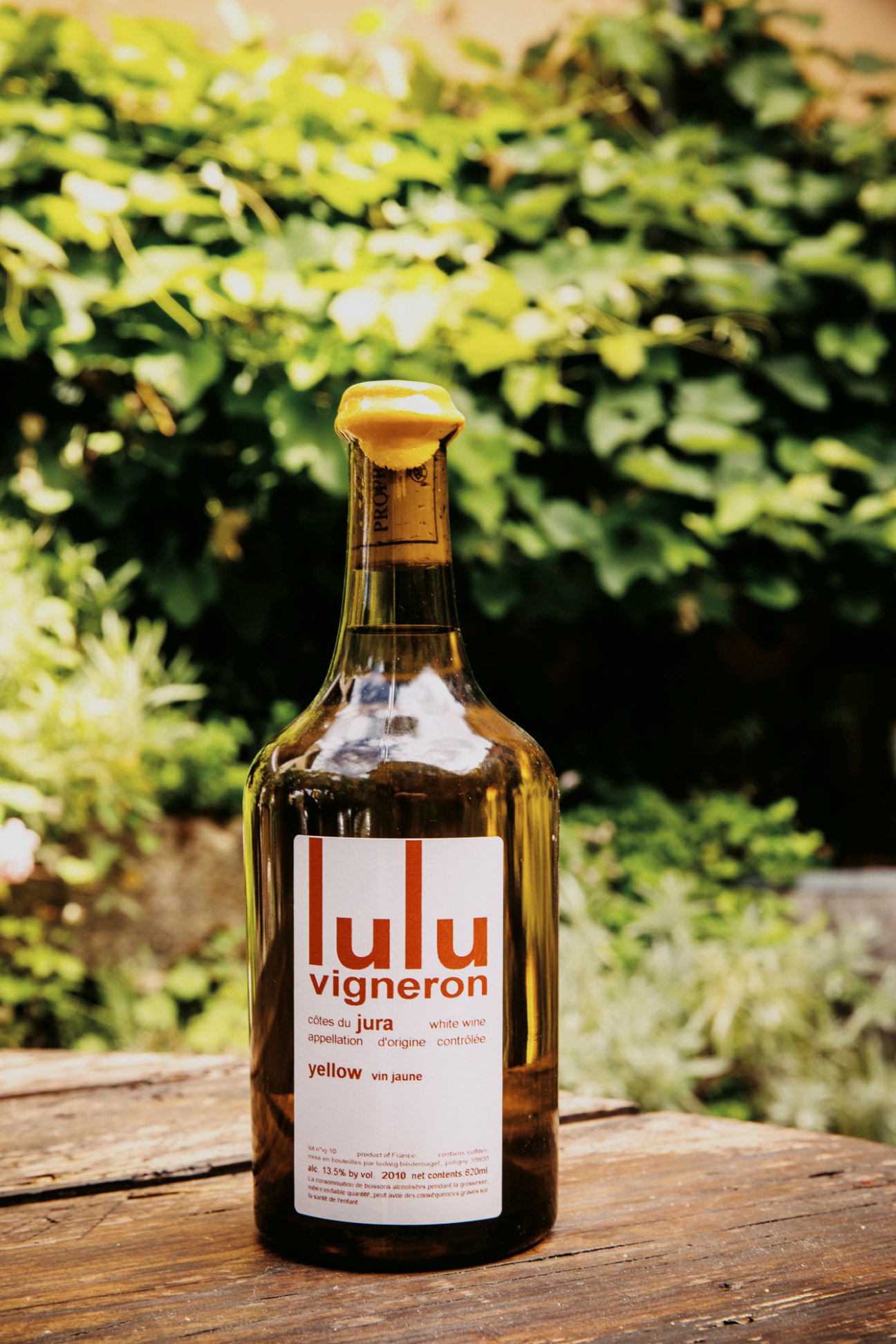 Bottle of Lulu Vigneron vin jaune yellow wine from the Jura region sitting on wooden surface with foliage in background