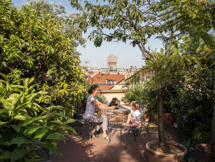 Woman and child at a table on a lush urban rooftop terrace.
