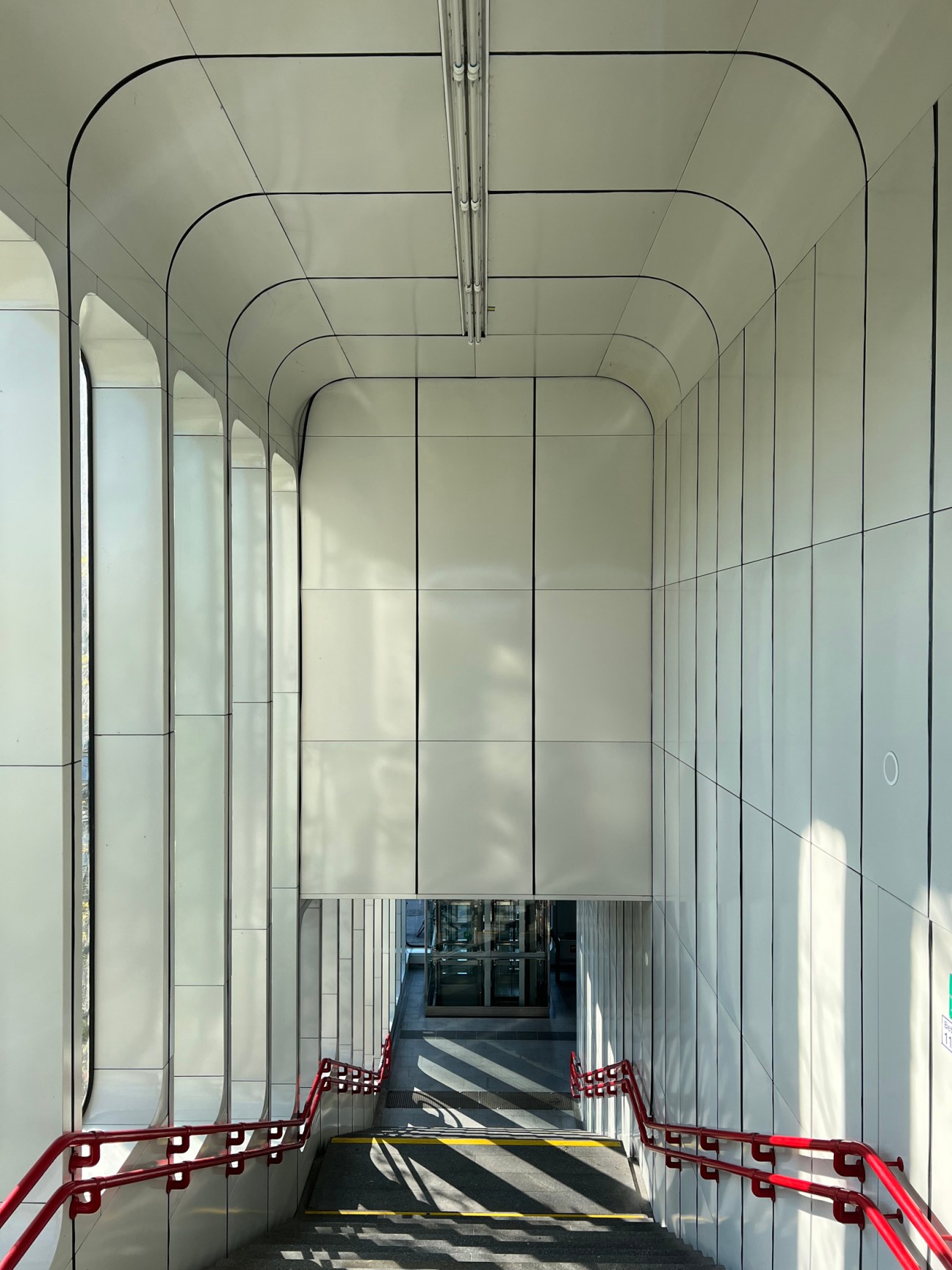 Modern subway station interior with curved white ceiling, geometric lines and red safety barriers