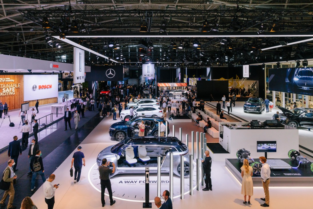 Wide view of the IAA Mobility motor show floor with multiple car displays and visitors walking through exhibition halls