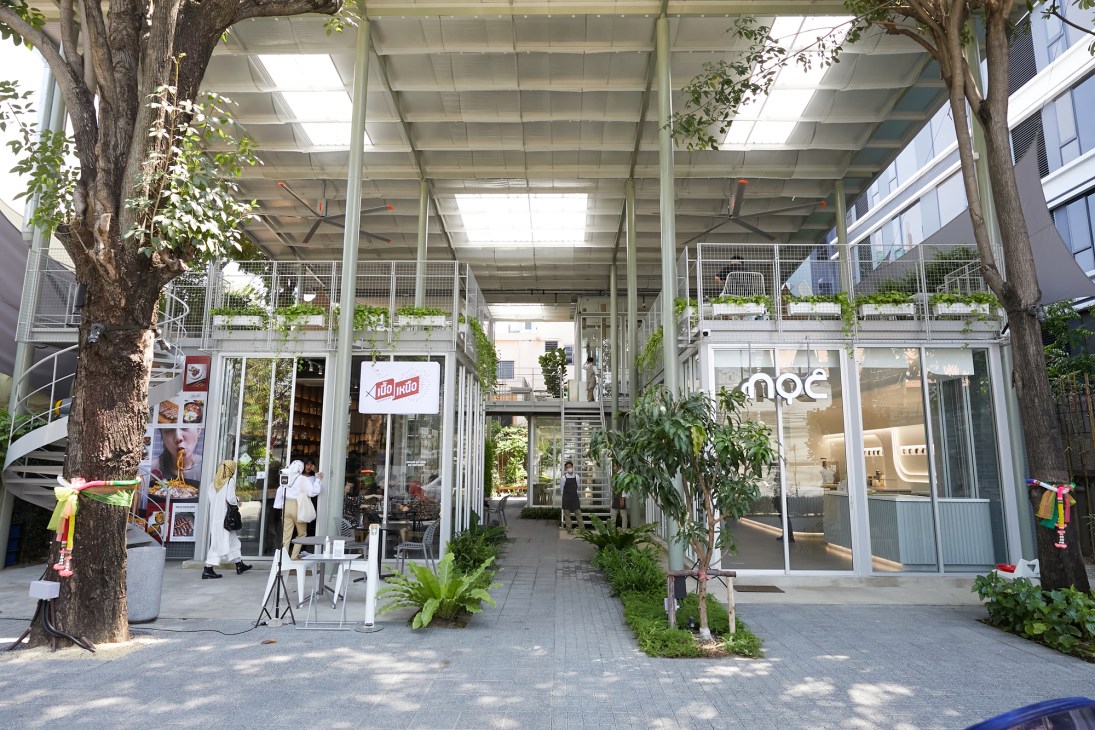 Powwowwow Community Mall in Bangkok features covered walkways with potted trees and retail storefronts under a metal-sheet roof.
