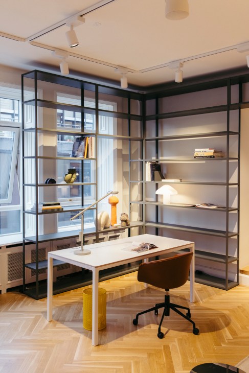 Modern office workspace with white desk, dark chair, yellow waste basket and built-in black metal shelving