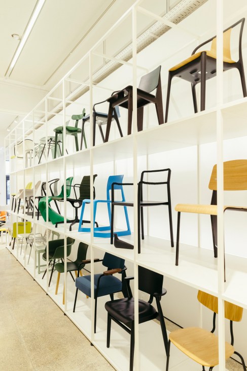 Display of various modern chairs arranged on white shelving in a minimalist showroom setting