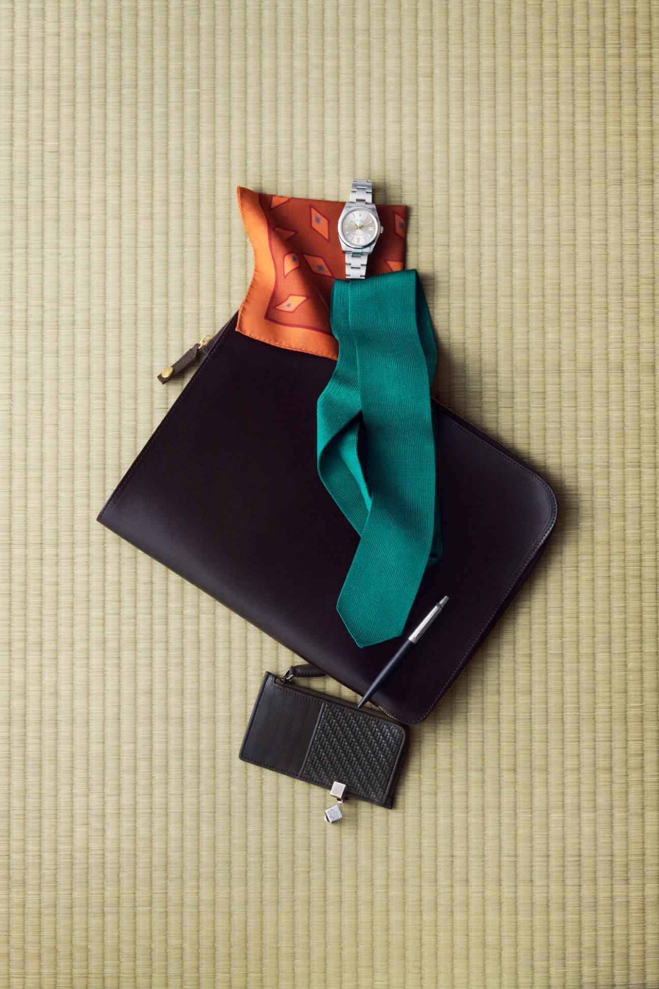 Business accessories arranged on tatami mat including watch, tie, briefcase, pen and card case