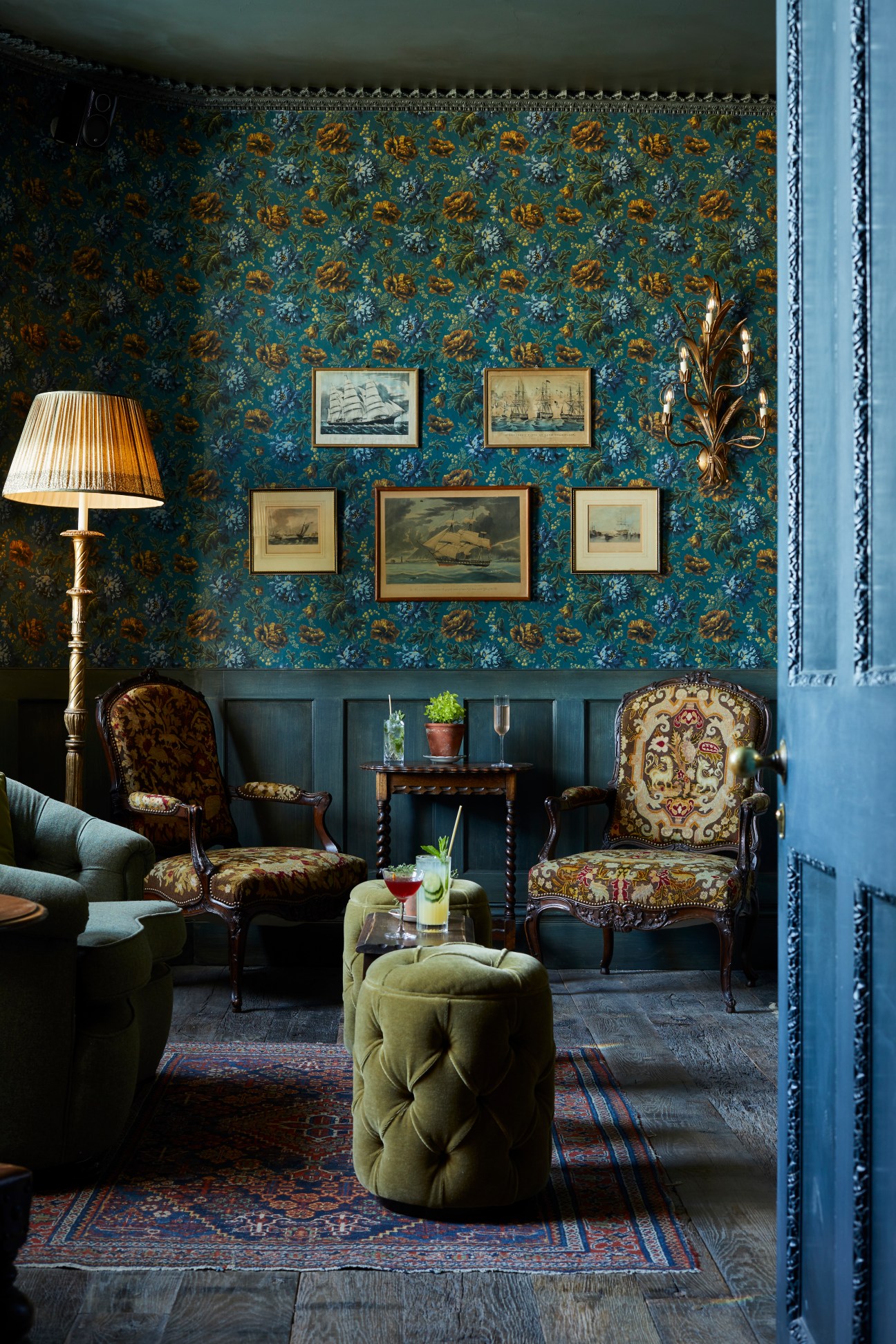 Elegant sitting room with blue floral wallpaper, nautical prints, antique chairs and brass sconce