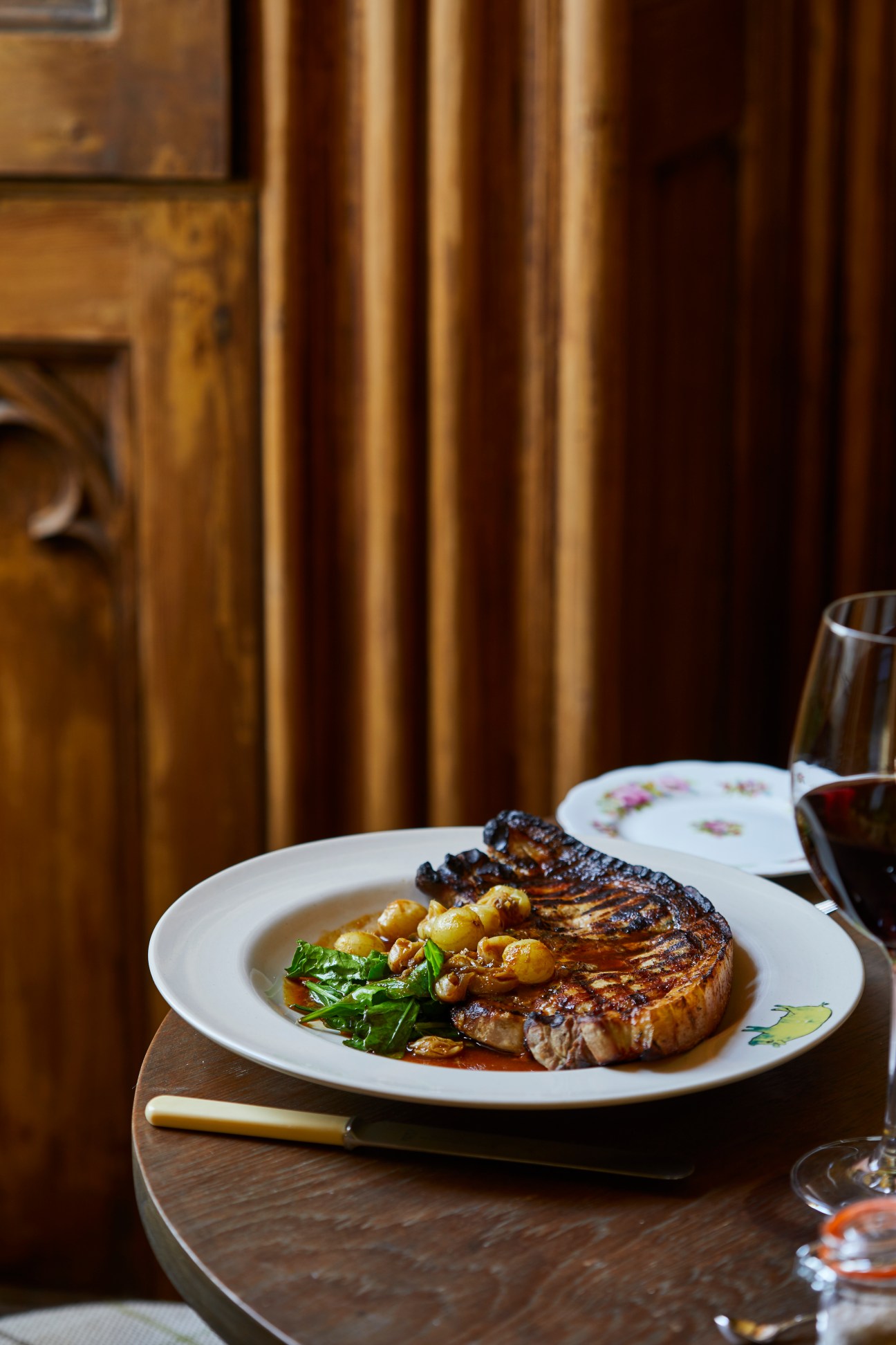 Grilled pork chop with grape garnish on floral plate beside wine glass