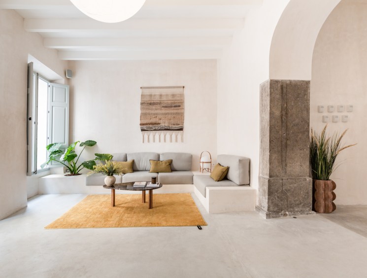 Modern minimalist living room with built-in grey sofa, mustard rug, and neutral stone archway