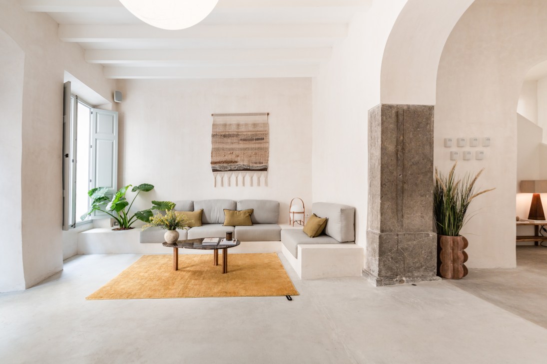 Modern minimalist living room with built-in grey sofa, mustard rug, and neutral stone archway