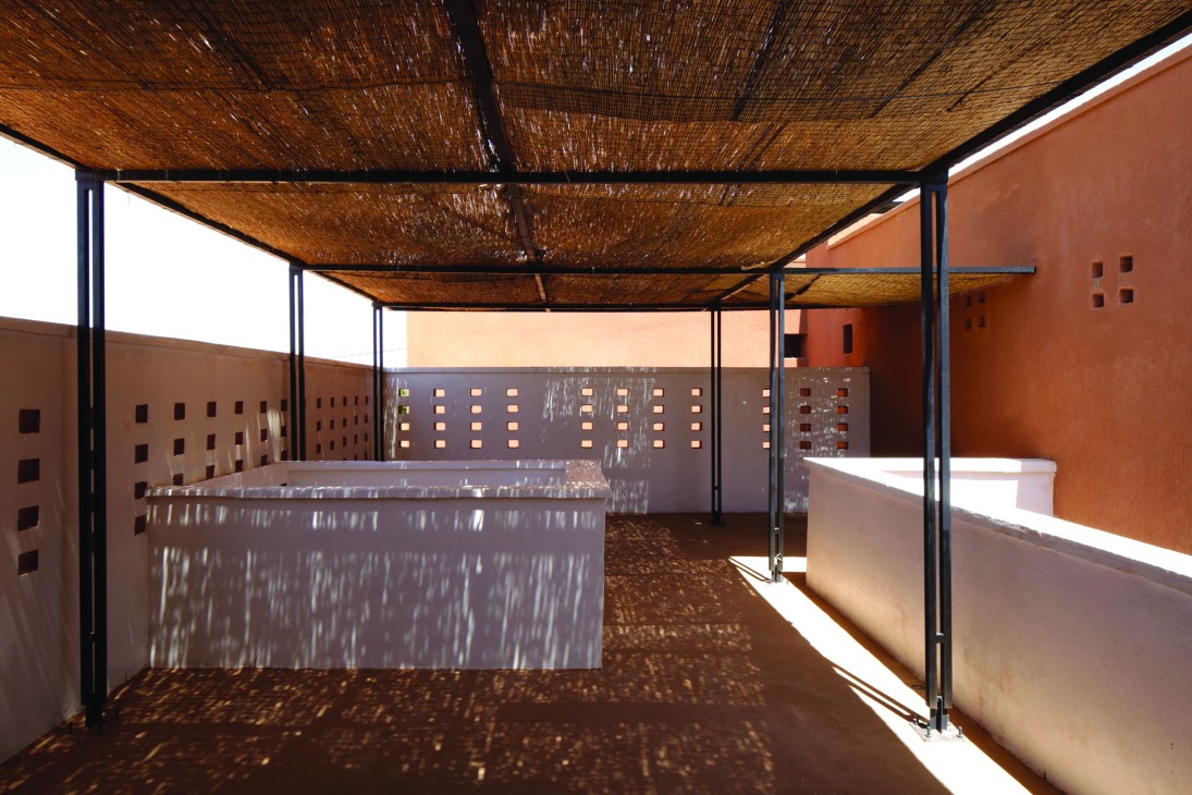 Covered outdoor terrace with woven bamboo canopy, concrete walls, and dappled sunlight patterns on the floor