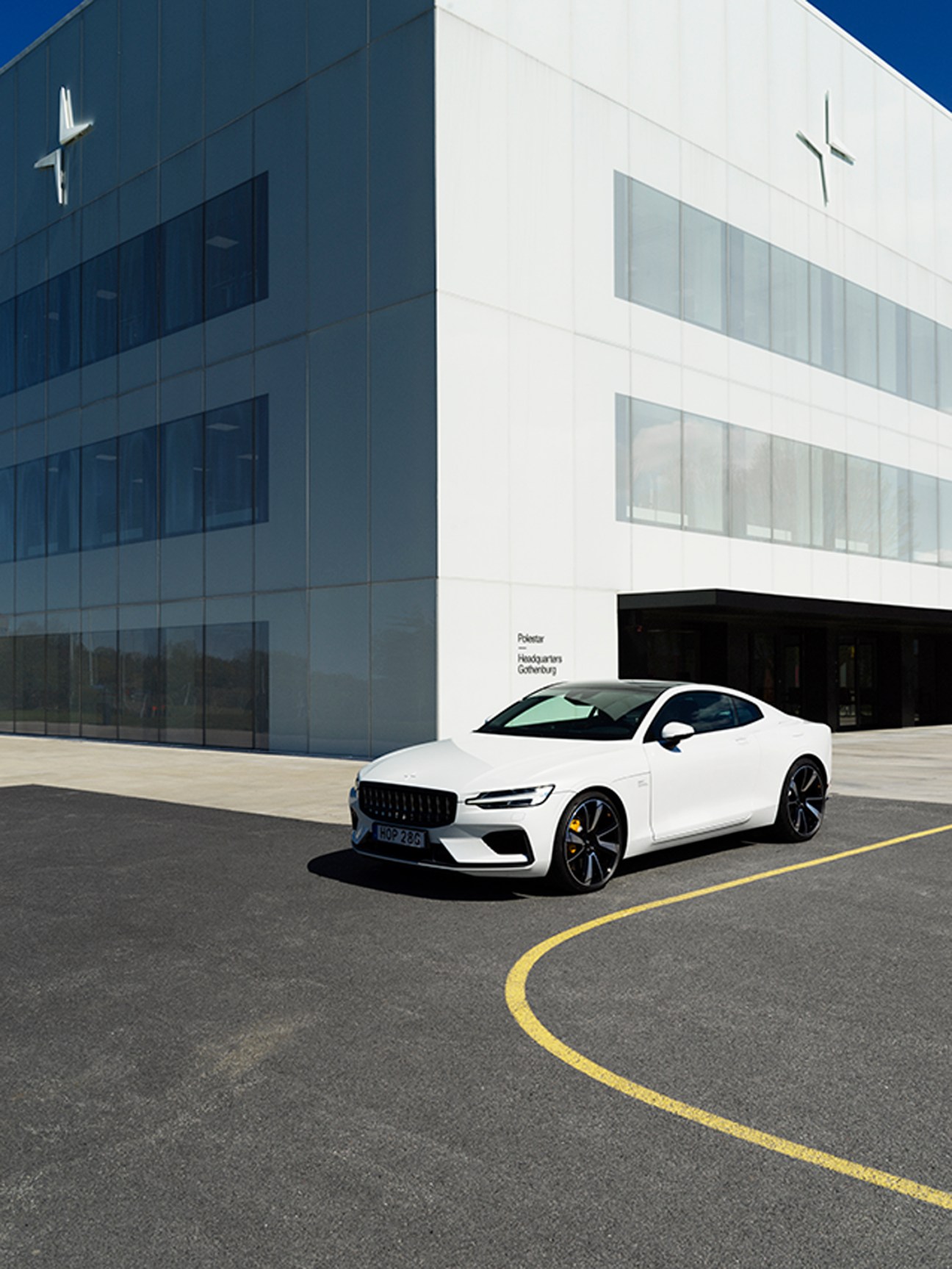 White Polestar electric car parked in front of modern building with yellow road markings