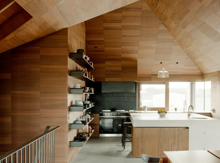 Open-plan kitchen with timber cabinetry, white island, green shelving and vaulted wood ceiling