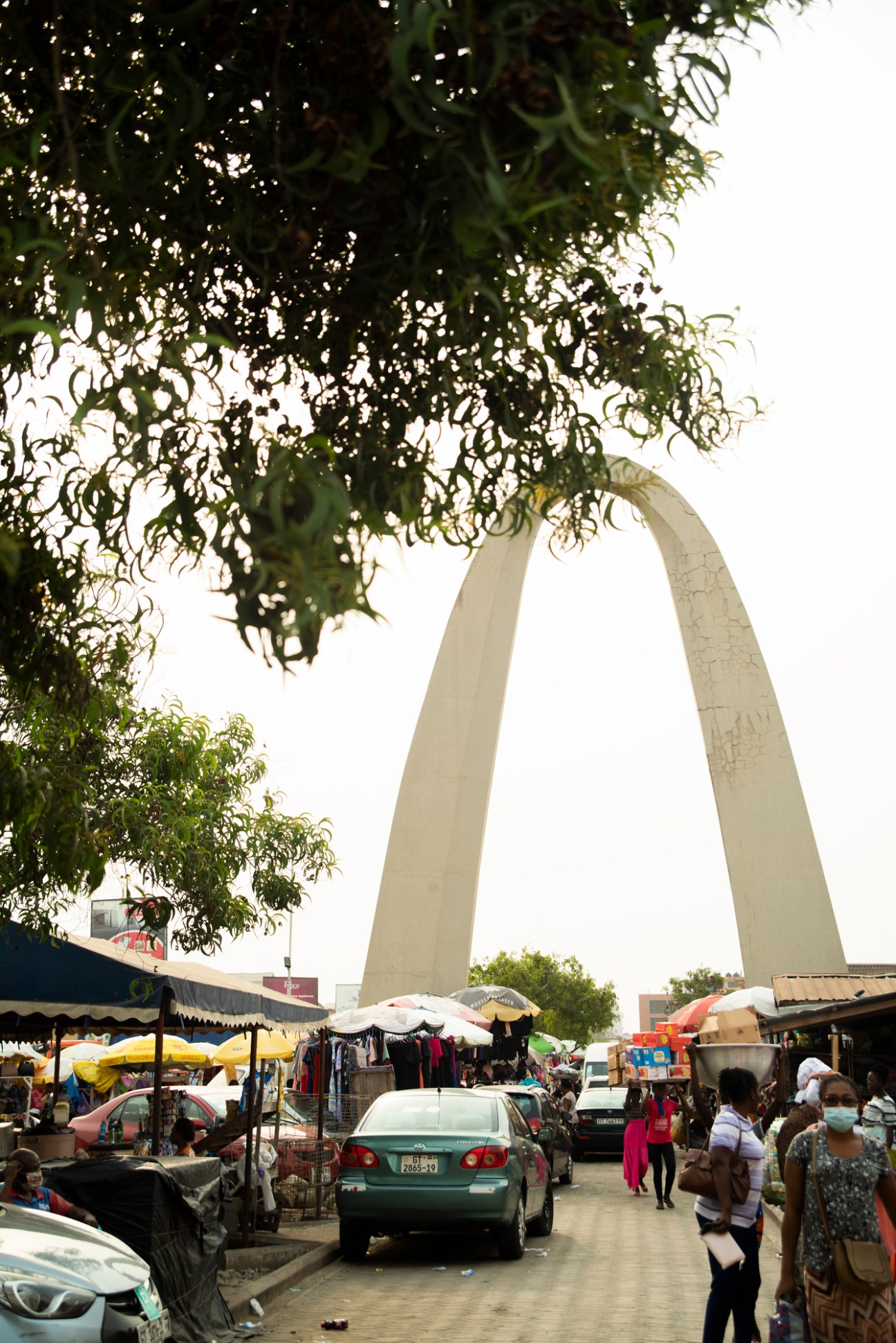 Busy street scene at Makola market in Accra with cars, vendors, shoppers and large concrete arch structure