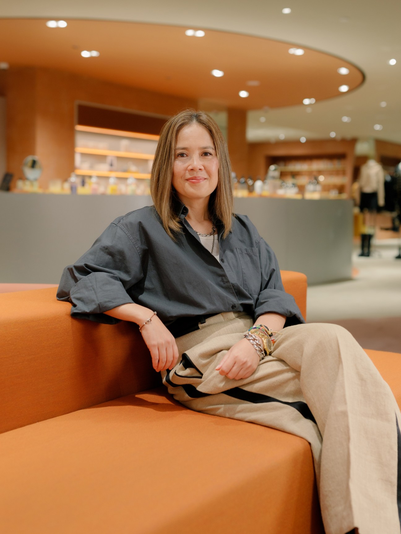 Blondie Tsang, president of Lane Crawford and Joyce, sits on an orange sofa in a modern retail space with warm lighting.