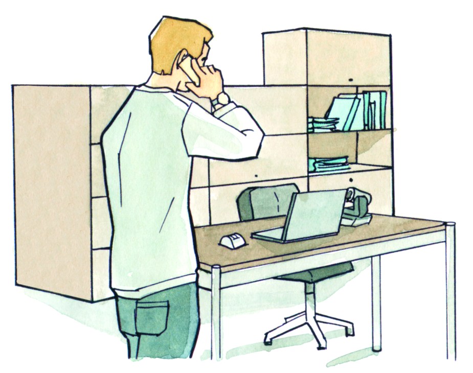 Man on phone standing next to desk with laptop and modular shelving system in office space