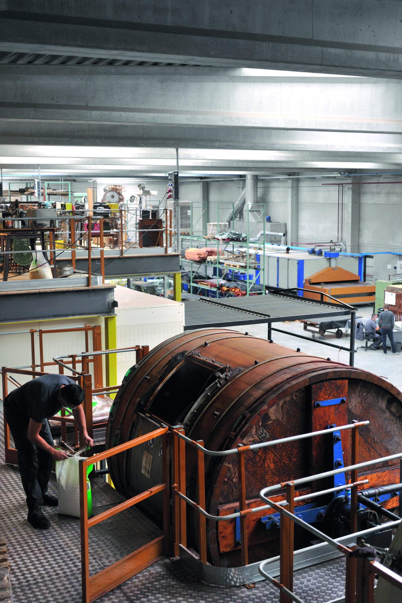 Large industrial leather processing drums in a modern tannery facility with worker operating machinery