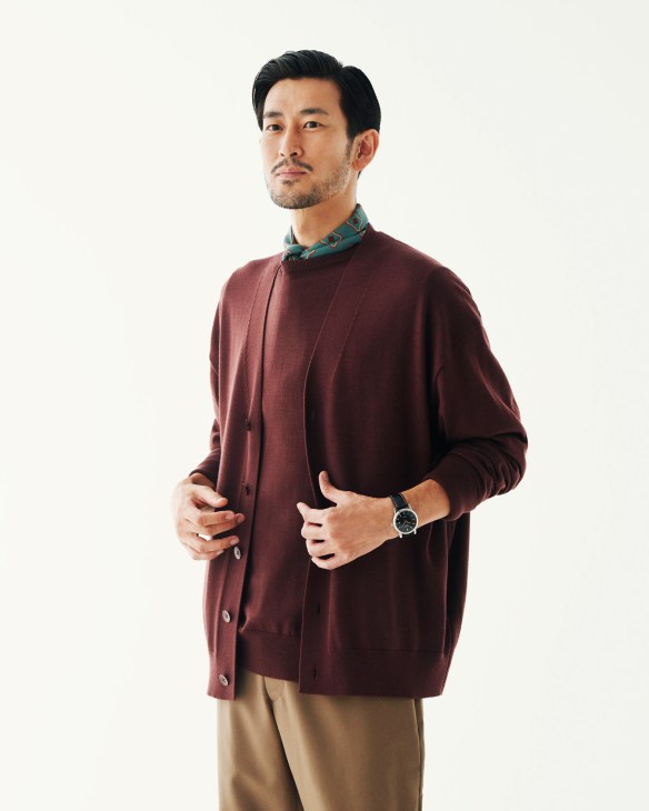 Man wearing burgundy cardigan over patterned scarf, beige trousers, and Longines watch.