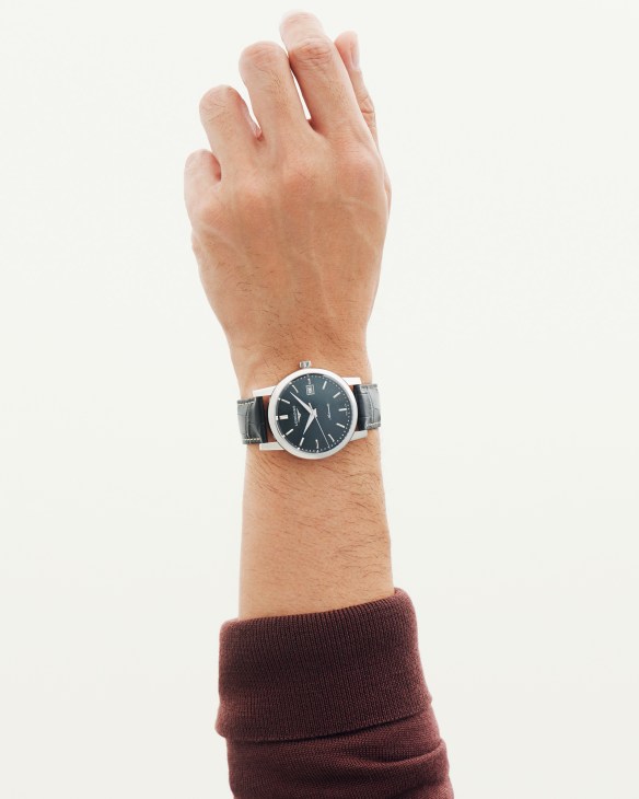 Hand wearing a Longines Master Collection watch with black dial and leather strap, burgundy cardigan cuff visible.