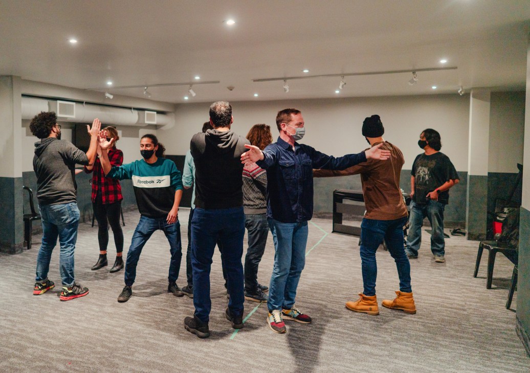 Group of masked people in casual clothing standing in a circle doing improv exercises in a modern classroom