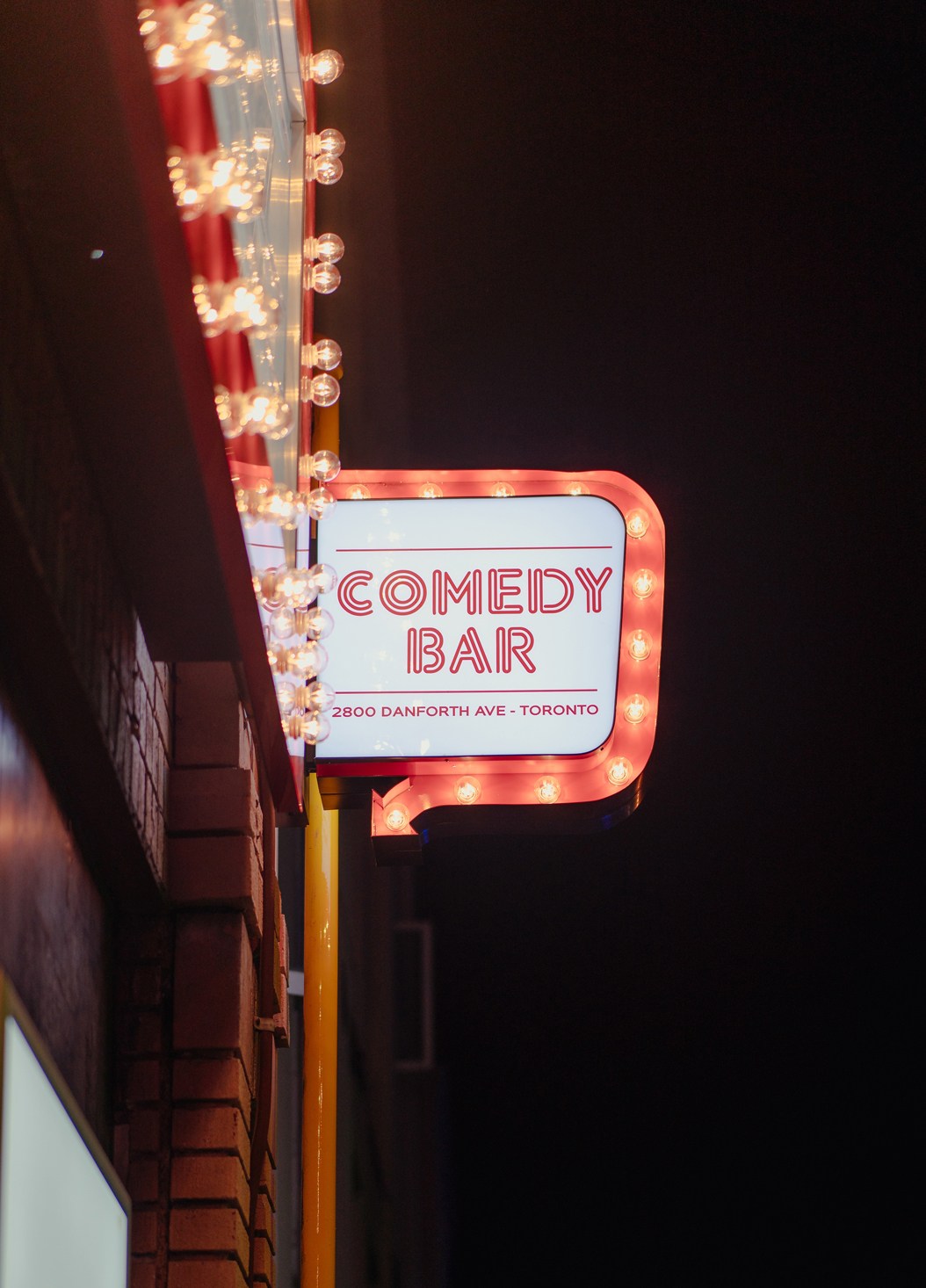 Illuminated Comedy Bar sign with marquee lights on Danforth Ave in Toronto
