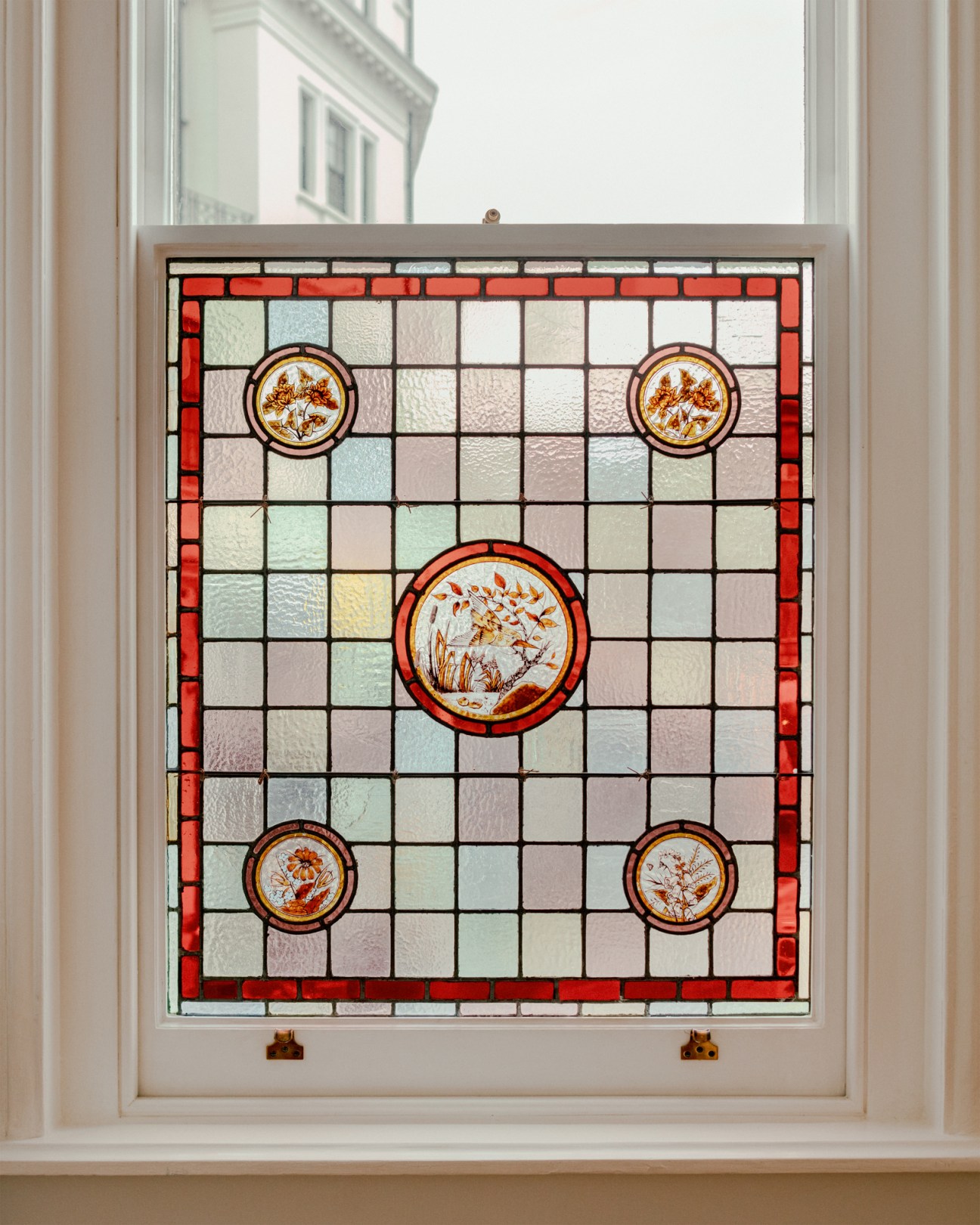 Victorian stained glass window with geometric pattern, red border, and five circular botanical motifs in ornate setting