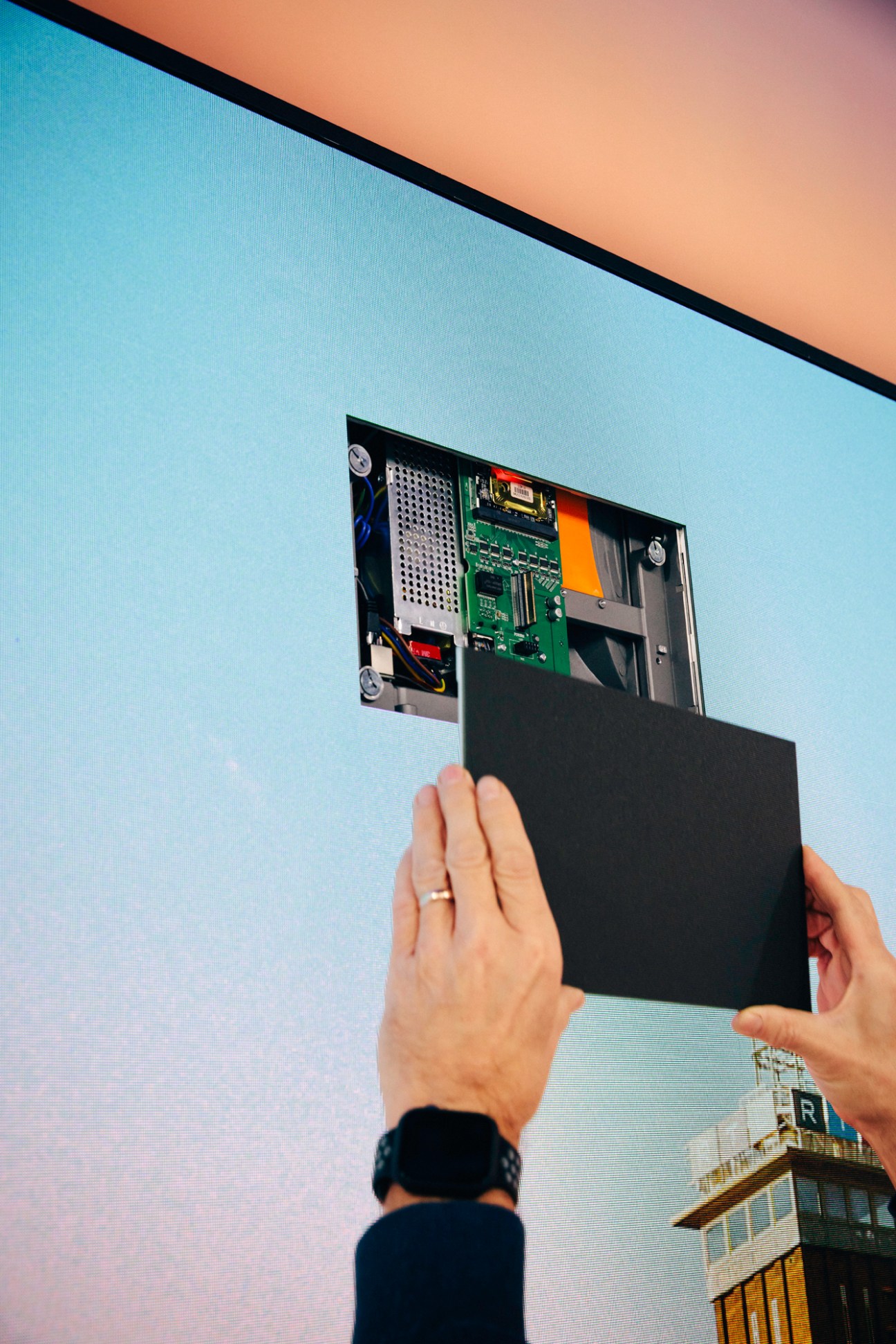 Hands inserting or removing a black rectangular device into an opening in a large display screen