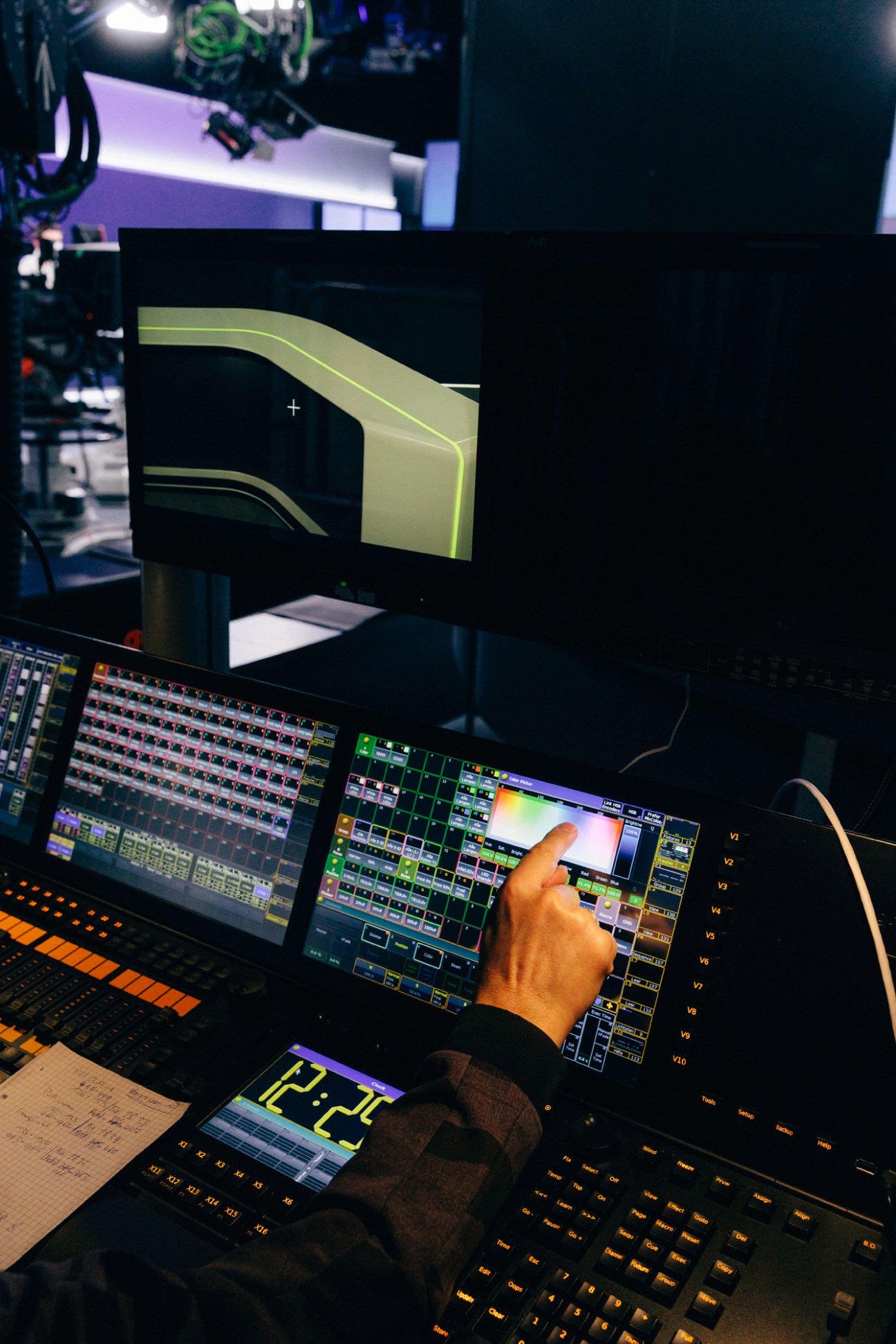 Person adjusting LED lighting controls at a broadcast studio control desk with multiple screens and equipment