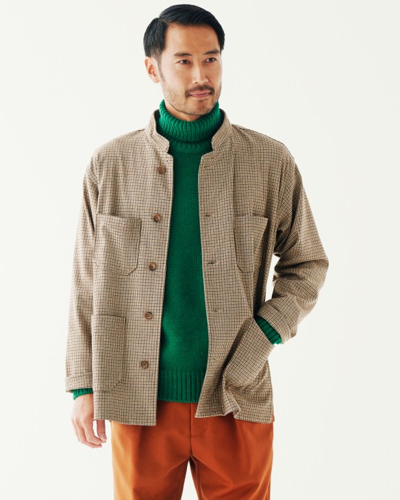Man wearing a beige checked Engineered Garments jacket over a green Brooksfield rollneck and rust-colored Tomorrowland trousers.
