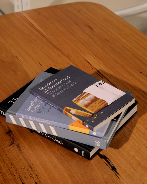 Stack of Broadsheet publications and cookbooks on wooden table.