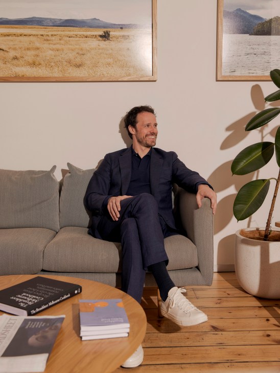 Nick Shelton, founder of Broadsheet media company, sits on a beige sofa in a modern office with framed landscape photographs on the wall behind him.