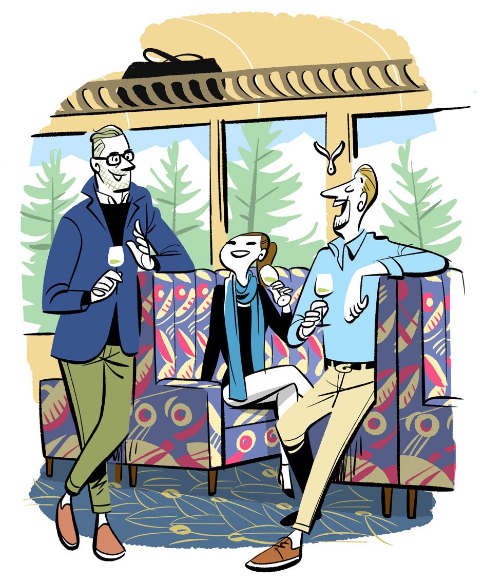 Two men in business casual attire sitting in colorful patterned train seats, holding wine glasses
