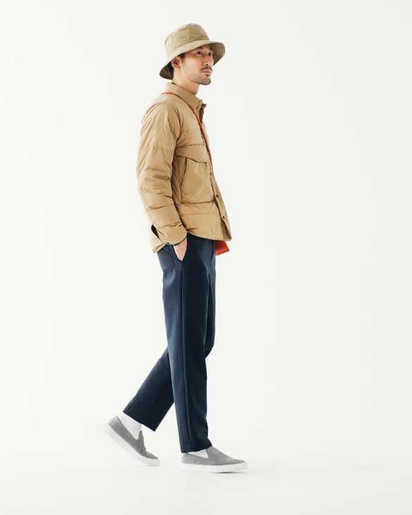 Man wearing a beige puffer jacket, navy trousers, and tan bucket hat against white background.