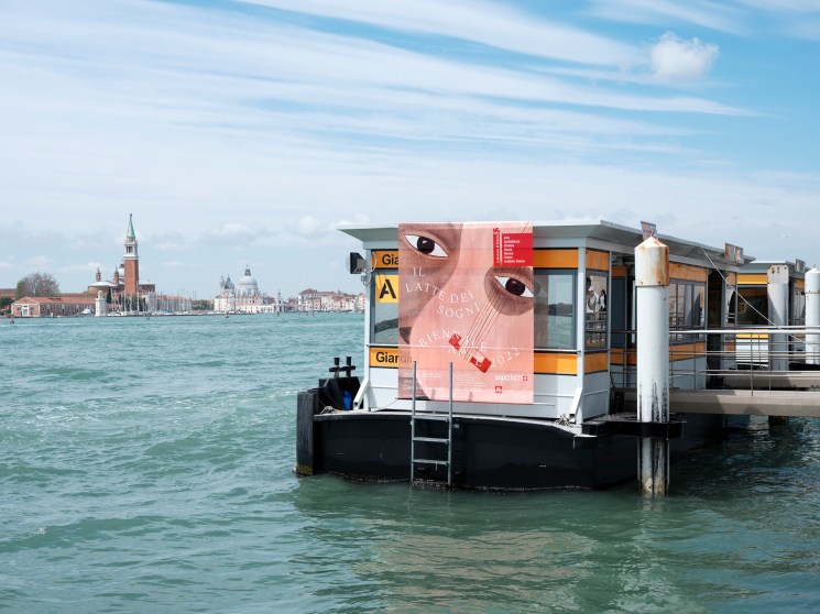 Venice Biennale poster with pink graphic design featuring stylized eyes on floating platform in Venice lagoon