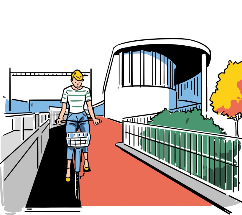 Person with bicycle walking on red cycling path through covered bridge structure with metal railings