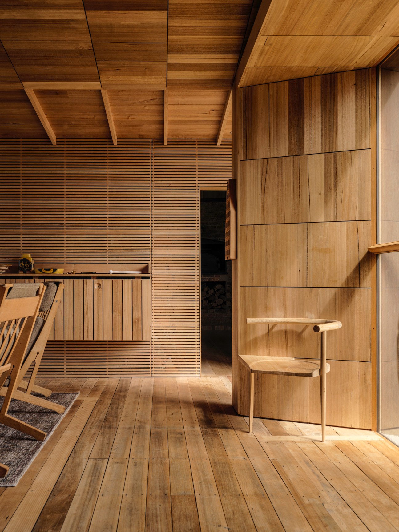 Interior room lined entirely in Tasmanian oak with retractable shutters, wooden ceiling beams, and a simple wooden chair.