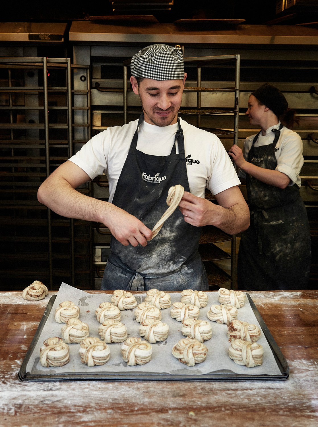 Baker Sherzod Baydadayev shaping dough in Fabrique's kitchen with another baker in background.