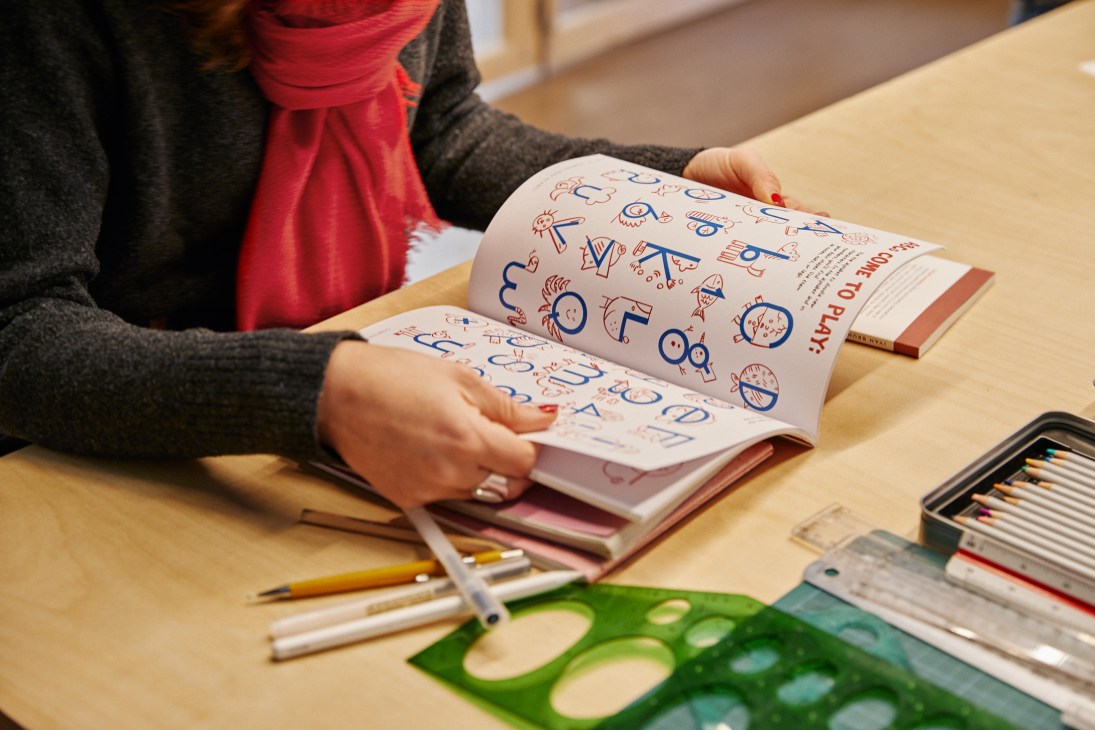 Student reading a comic book at La Gossa school with art supplies and materials spread on wooden table