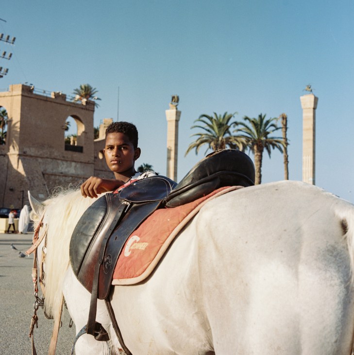 Young person on horseback in front of historic architecture with palm trees and columns in Tripoli