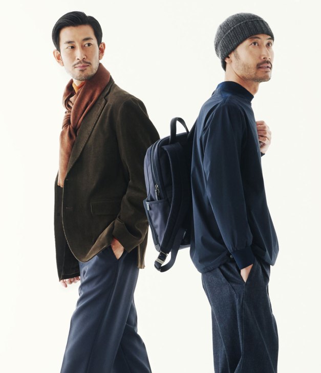 Two men wearing layered outfits with jackets, scarves, and backpacks against a white background.