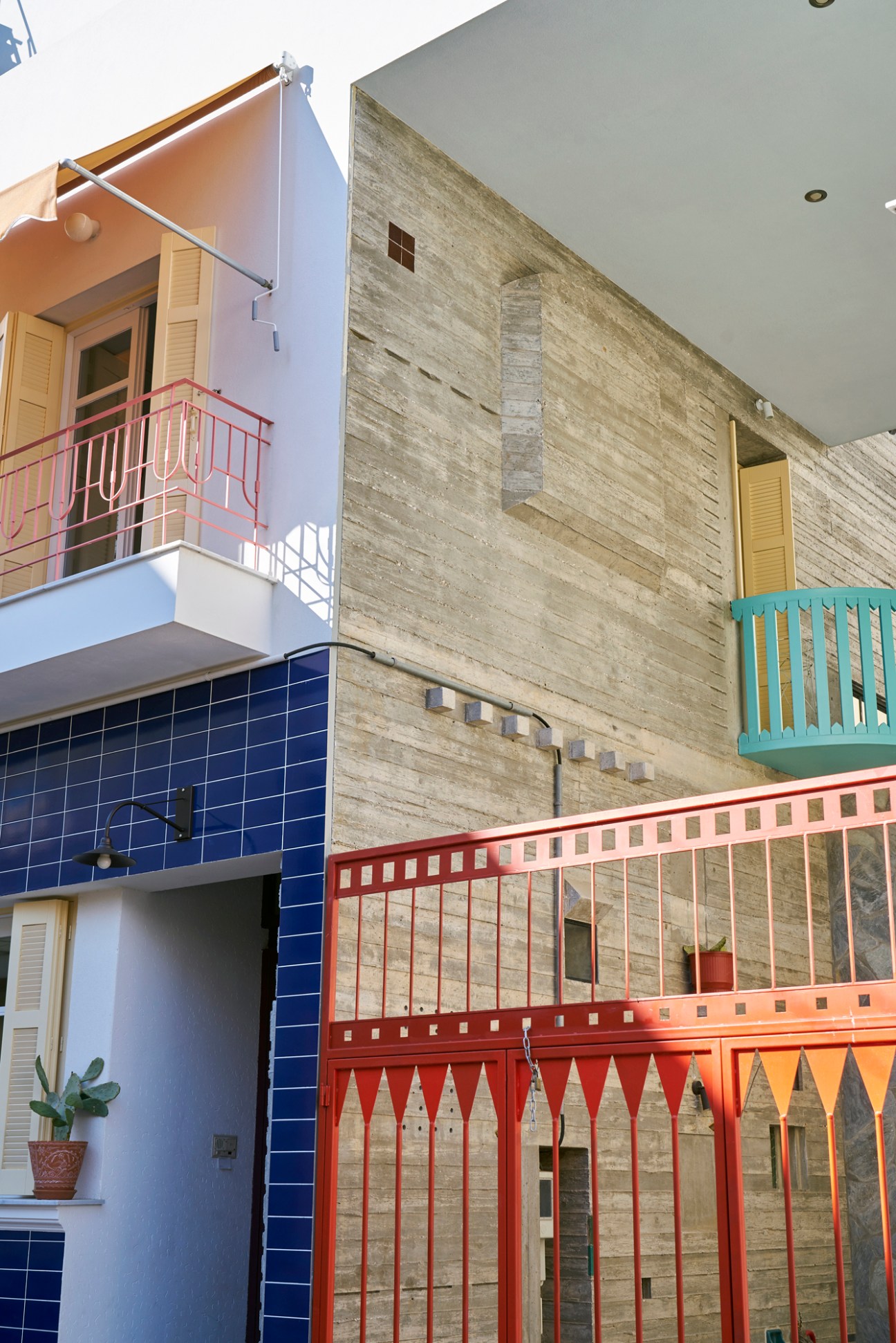 Colorful modern building exterior featuring blue tile cladding on the lower level, concrete walls, and distinctive colored railings (pink, turquoise, red, and orange) on multiple balconies in Athens.