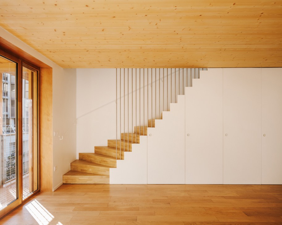 Interior staircase with light wood steps, white walls, vertical slat railing and built-in storage underneath